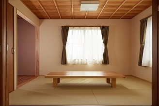グリーンのカーテンの窓2つと長方形のテーブルがある和室です。